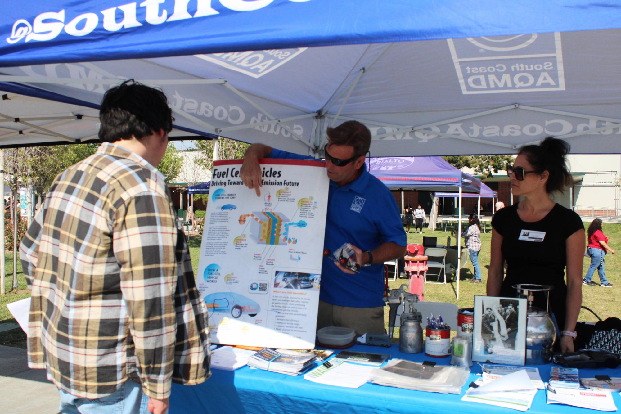 Eric Tapia listens to Todel Warden and Cathy Bartels from (SCAQMD) about Hydrogen fuel cells being used in cars.